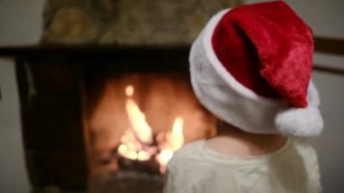 Noel Baba şapkalı çocuk şöminenin yanında.