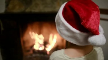 Noel Baba şapkalı çocuk şöminenin yanında.