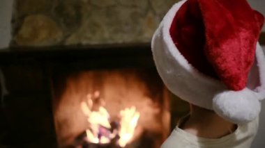 Noel Baba şapkalı çocuk şöminenin yanında.