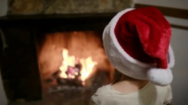 Noel Baba şapkalı çocuk şöminenin yanında.