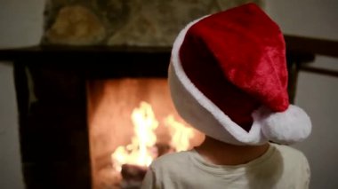 Noel Baba şapkalı çocuk şöminenin yanında.