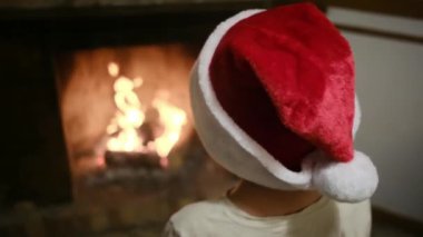 Noel Baba şapkalı çocuk şöminenin yanında.