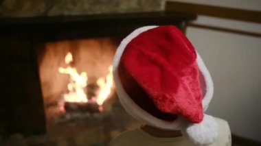 Noel Baba şapkalı çocuk şöminenin yanında.
