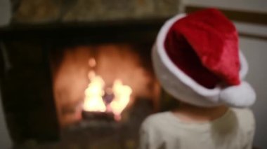 Noel Baba şapkalı çocuk şöminenin yanında.