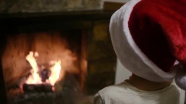 Noel Baba şapkalı çocuk şöminenin yanında.