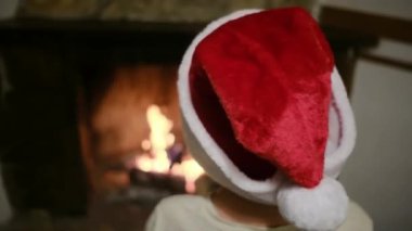 Noel Baba şapkalı çocuk şöminenin yanında.