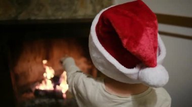 Noel Baba şapkalı çocuk şöminenin yanında.