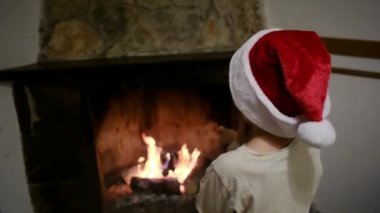 Noel Baba şapkalı çocuk şöminenin yanında.