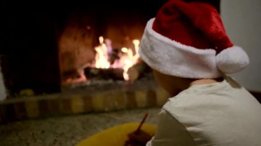 Noel Baba şapkalı çocuk şöminenin yanındaki Noel Baba 'ya mektup yazıyor.