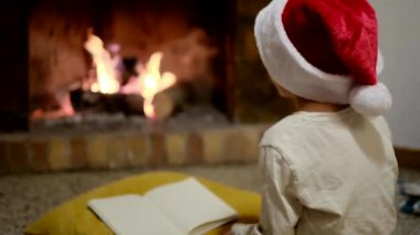 Noel Baba şapkalı çocuk şöminenin yanındaki Noel Baba 'ya mektup yazıyor.