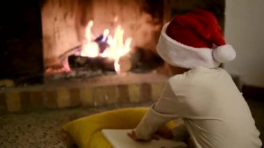 Noel Baba şapkalı çocuk şöminenin yanındaki Noel Baba 'ya mektup yazıyor.