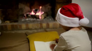 Noel Baba şapkalı çocuk şöminenin yanındaki Noel Baba 'ya mektup yazıyor.