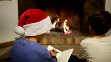 Çocuklar Noel 'i şömineyle kutluyor. Çocuk Noel Baba 'ya mektup yazıyor.
