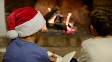 Çocuklar Noel 'i şömineyle kutluyor. Çocuk Noel Baba 'ya mektup yazıyor.