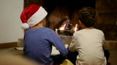 Çocuklar Noel 'i şömineyle kutluyor. Çocuk Noel Baba 'ya mektup yazıyor.