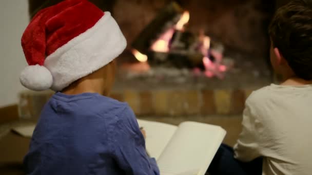 暖炉でクリスマスを祝う子供たち サンタに手紙を書く少年 — ストック動画