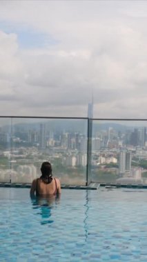 şehir silueti üzerinde sonsuz havuzda yüzen seyahat eden bir kadın. 