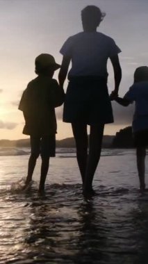 Aile bağının yürek ısıtan özünü bir annenin ve oğullarının sakin bir sahilde büyüleyici bir gün batımının arka planında el ele tutuşmaları gibi yaşayın.