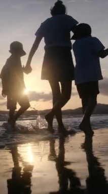 Aile bağının yürek ısıtan özünü bir annenin ve oğullarının sakin bir sahilde büyüleyici bir gün batımının arka planında el ele tutuşmaları gibi yaşayın.