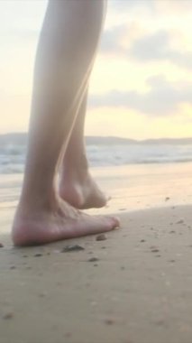  Yaz tatilinde ya da tatilde kadın bacakları deniz kenarında kumda. Sahilde, doğada ve özgürlükte bir kadın tek başına akıntıda, gelgitte ya da dalgalarda yürür.