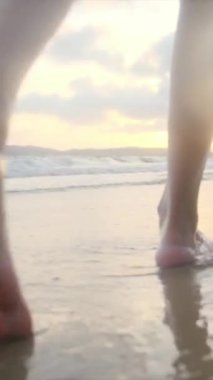  Yaz tatilinde ya da tatilde kadın bacakları deniz kenarında kumda. Sahilde, doğada ve özgürlükte bir kadın tek başına akıntıda, gelgitte ya da dalgalarda yürür.