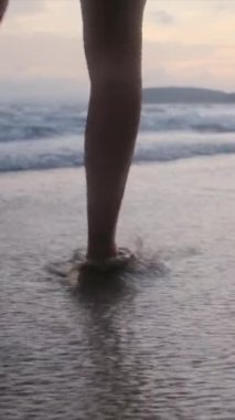  Yaz tatili ya da tatil boyunca kadın bacakları kumda okyanus ya da deniz kenarında yürüyor. Sahilde, doğada ve özgürlükte bir kadın tek başına akıntıda, gelgitte ya da dalgalarda yürür.