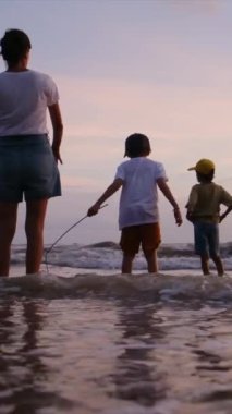 Gün batımında sahilde oğulları olan genç bir kadının siluetleri.