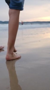 Kadın ve çocuk kumsalda yalınayak yürüyor.