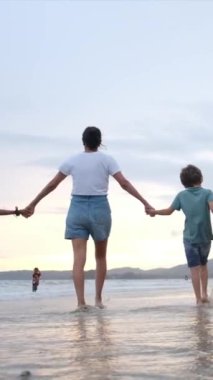 Gün batımında sahilde oğulları olan genç bir kadının siluetleri.