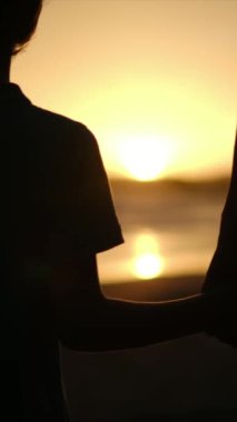 Aile bağının yürek ısıtan özünü, sakin bir sahilde büyüleyici bir günbatımının arka planına karşı el ele tutuşan bir anne ve oğlunun silueti gibi yaşayın.