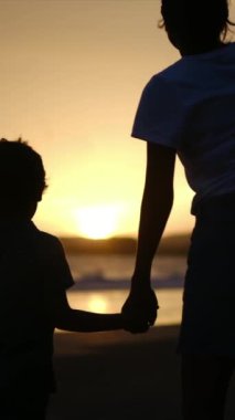 Aile bağının yürek ısıtan özünü, sakin bir sahilde büyüleyici bir günbatımının arka planına karşı el ele tutuşan bir anne ve oğlunun silueti gibi yaşayın.