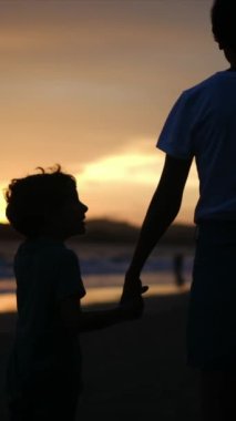 Aile bağının yürek ısıtan özünü, sakin bir sahilde büyüleyici bir günbatımının arka planına karşı el ele tutuşan bir anne ve oğlunun silueti gibi yaşayın.
