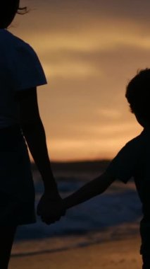 Aile bağının yürek ısıtan özünü, sakin bir sahilde büyüleyici bir günbatımının arka planına karşı el ele tutuşan bir anne ve oğlunun silueti gibi yaşayın.