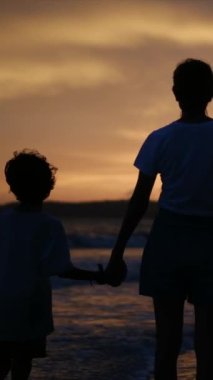 Aile bağının yürek ısıtan özünü, sakin bir sahilde büyüleyici bir günbatımının arka planına karşı el ele tutuşan bir anne ve oğlunun silueti gibi yaşayın.