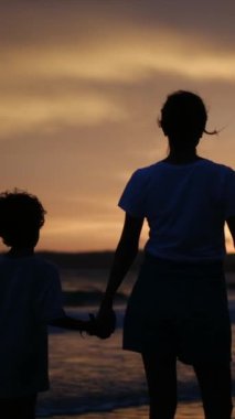Aile bağının yürek ısıtan özünü, sakin bir sahilde büyüleyici bir günbatımının arka planına karşı el ele tutuşan bir anne ve oğlunun silueti gibi yaşayın.