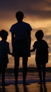 Aile bağının yürek ısıtan özünü bir annenin ve oğullarının sakin bir sahilde büyüleyici bir gün batımının arka planında el ele tutuşmaları gibi yaşayın.