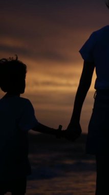 Aile bağının yürek ısıtan özünü, sakin bir sahilde büyüleyici bir günbatımının arka planına karşı el ele tutuşan bir anne ve oğlunun silueti gibi yaşayın.