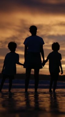 Aile bağının yürek ısıtan özünü bir annenin ve oğullarının sakin bir sahilde büyüleyici bir gün batımının arka planında el ele tutuşmaları gibi yaşayın.