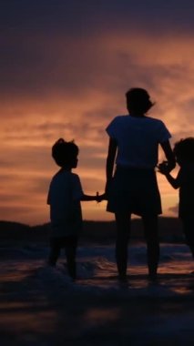 Aile bağının yürek ısıtan özünü bir annenin ve oğullarının sakin bir sahilde büyüleyici bir gün batımının arka planında el ele tutuşmaları gibi yaşayın.