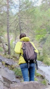 Dağlarda yürüyüş yapan kadın şelaleye bakıyor. 