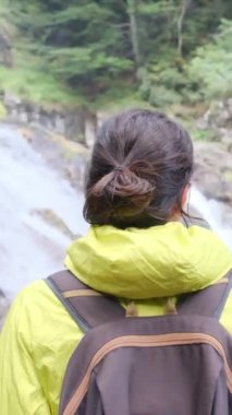 Dağlarda yürüyüş yapan kadın şelaleye bakıyor. 