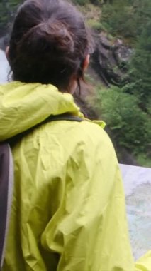 Dağlarda yürüyüş yapan kadın şelalenin yakınındaki haritaya bakıyor. 