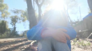 Üzgün çocuk dışarıda, dizlerinin üzerinde oturuyor.