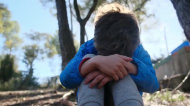 Üzgün çocuk dışarıda, dizlerinin üzerinde oturuyor.
