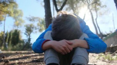 Üzgün çocuk dışarıda, dizlerinin üzerinde oturuyor.