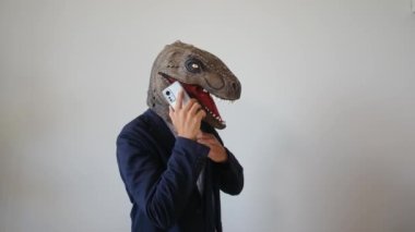 Akıllı telefonlu dinozor maskeli bir iş adamı.
