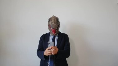 Akıllı telefonlu dinozor maskeli bir iş adamı.