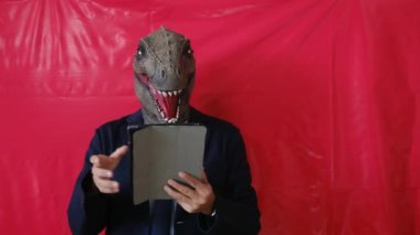 Dinozor maskeli iş adamı stüdyoda tablet bilgisayar tutuyor.