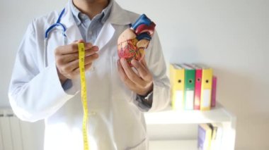Doktor kalp modelini tutuyor ve hastane, sağlık ve sağlık hizmetleri konseptinde şerit ölçüyor.