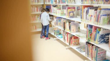 Küçük çocuklar kütüphanede kitap seçiyor.